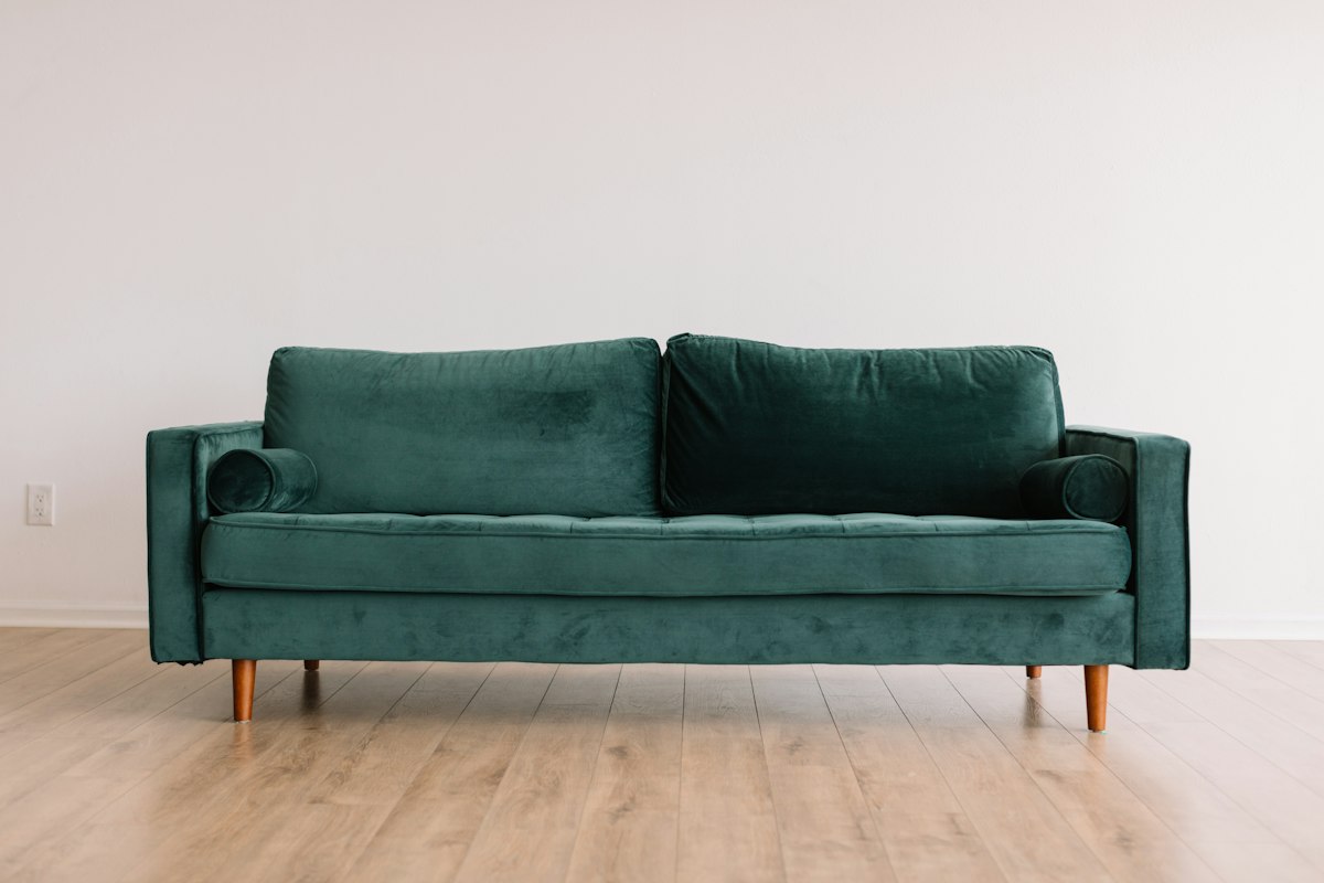 Cozy modern living room photograph with a plush neutral sofa, layered cushions, warm wooden coffee table, soft natural light through large windows, indoor plants and textured rug, inviting and elegant, no people